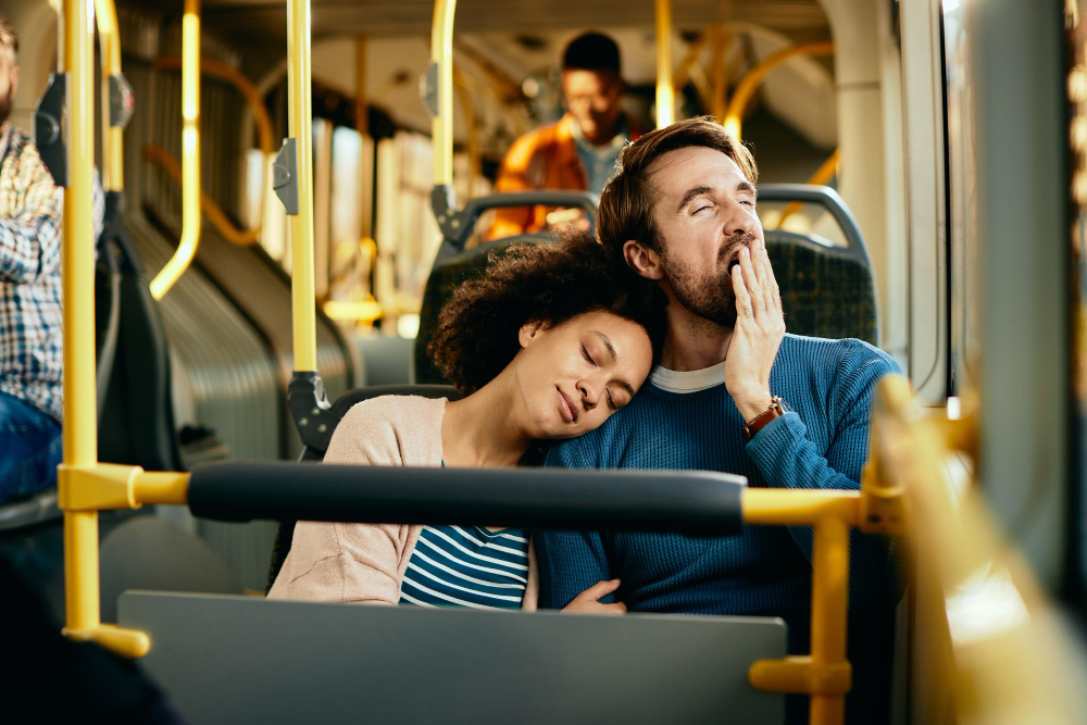 אישה נשענת בעיניים עצומות על כתפו של גבר מפהק במושב אוטובוס